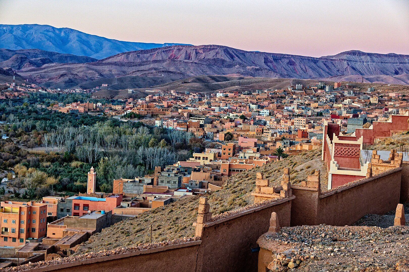 Panorama di una città con edifici in terracotta incastonata in una valle, con aspre montagne che si ergono sullo sfondo al crepuscolo.