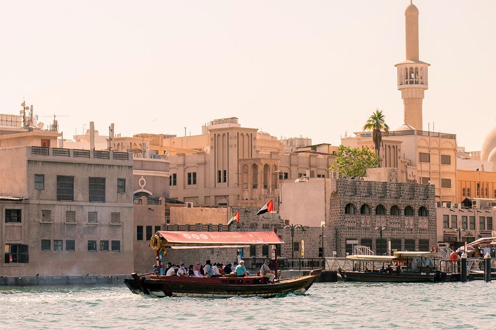 Eine WeRoad Gruppenreise segelt auf einem traditionellen Holzboot vorbei an einer Stadtansicht mit einem markanten Minarett im Hintergrund.