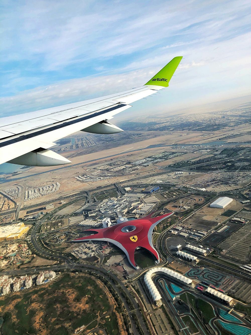 Eine Luftaufnahme aus einem Flugzeug, die seine Tragfläche über einer ausgedehnten Stadtlandschaft mit einem großen, roten, sternförmigen Gebäude zeigt.