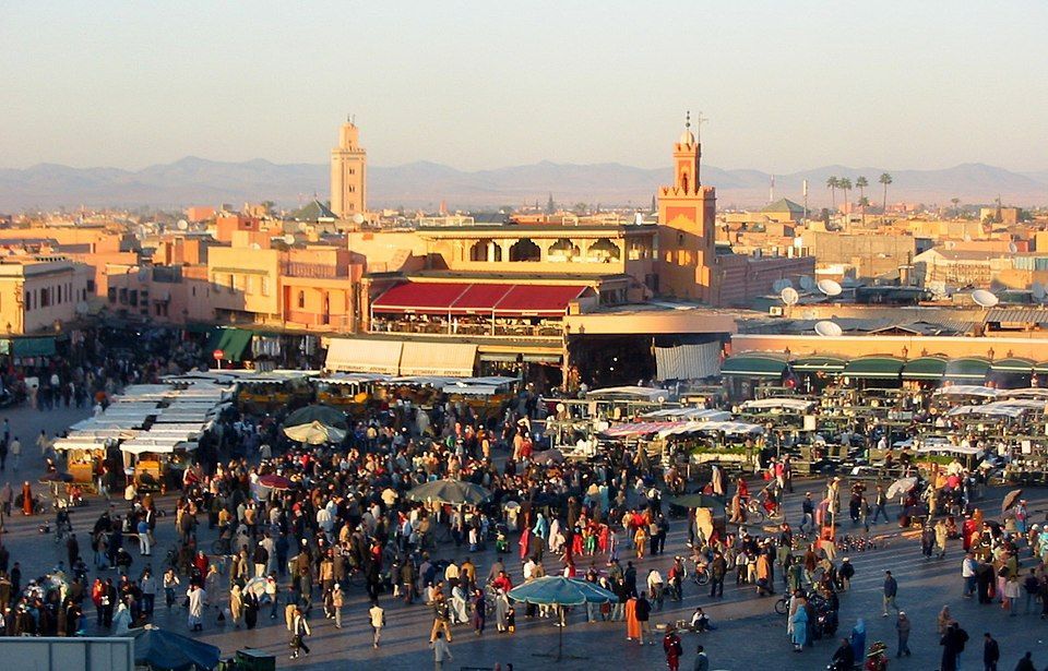 Vista panoramica di una vivace piazza cittadina, affollata di gente e bancarelle, all'ora d'oro.