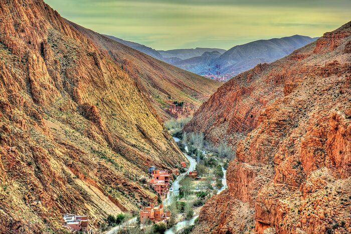 Una vista su un canyon profondo e roccioso, dove una strada e un fiume si snodano tra piccoli villaggi con edifici rosso mattone.