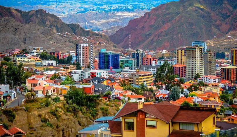 Un paesaggio urbano vivace con un mix di grattacieli e case, incastonato in una valle tra aspre montagne bruno-rossastre.