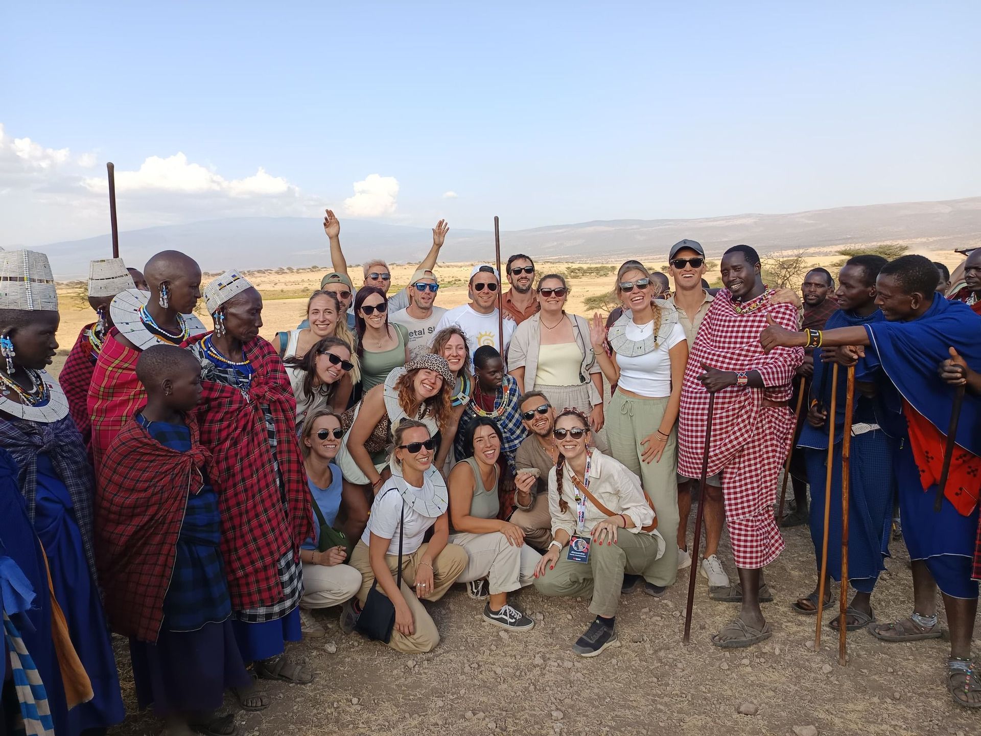 Un gruppo WeRoad in viaggio posa per una foto di gruppo con membri di tribù locali in abiti tradizionali, in un paesaggio di savana.