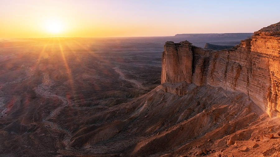 Il sole al tramonto tinge d'oro un vasto canyon desertico con ripide scogliere rocciose.
