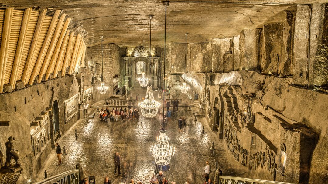 Una vasta sala sotterranea scavata nella roccia, illuminata da diversi grandi lampadari, mentre i visitatori camminano sul pavimento lucido.