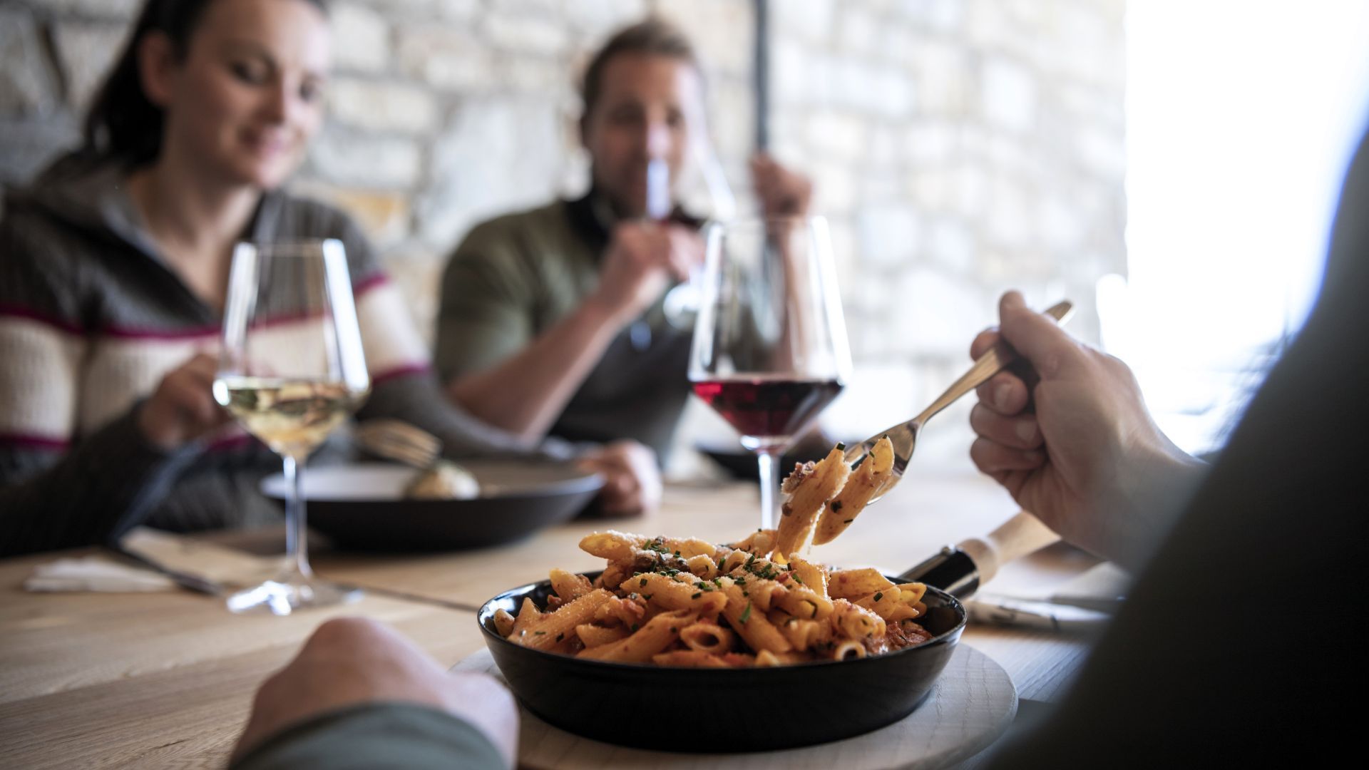 Mitglieder einer WeRoad-Gruppenreise genießen Penne-Pasta und Wein an einem rustikalen Restauranttisch.