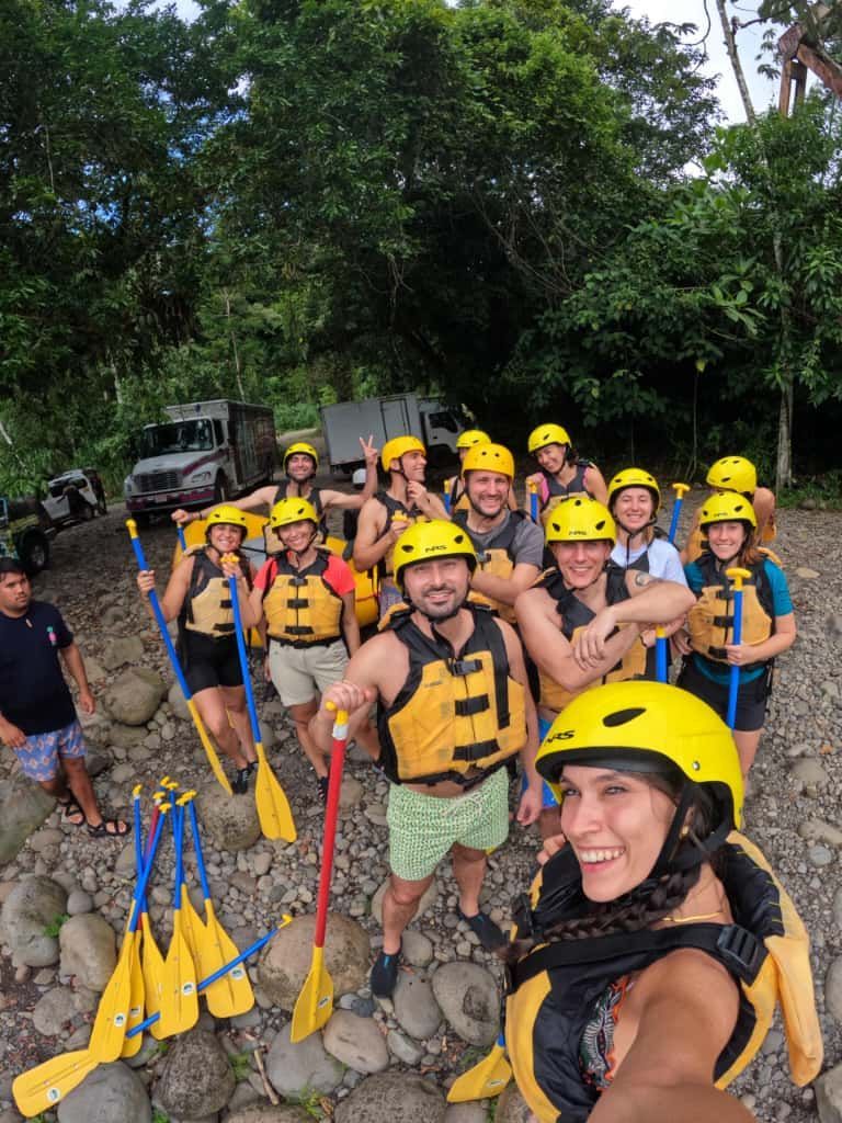 Un gruppo WeRoad con caschi gialli e giubbotti di salvataggio posa per un selfie sulla riva rocciosa di un fiume prima di fare rafting.