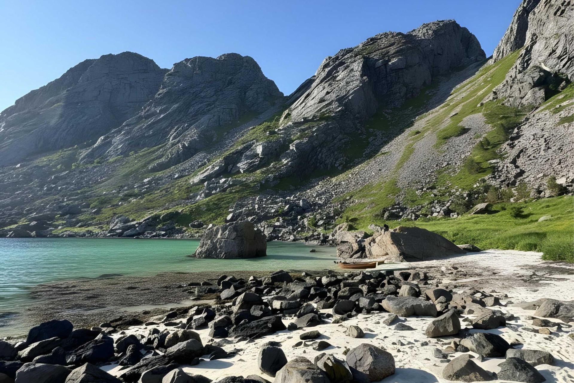 Ein felsiger Strand mit einem kleinen Holzboot trifft auf ruhiges türkisfarbenes Wasser am Fuße steiler Berge unter einem klaren blauen Himmel.