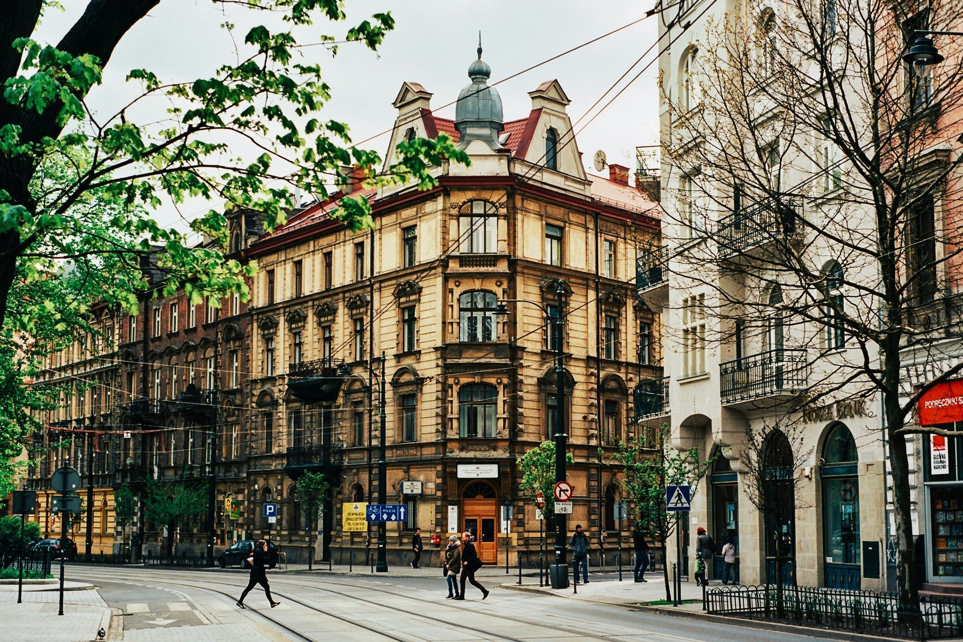 Un edificio de esquina ornamentado en una calle de la ciudad con vías de tranvía y peatones cruzando en una intersección.