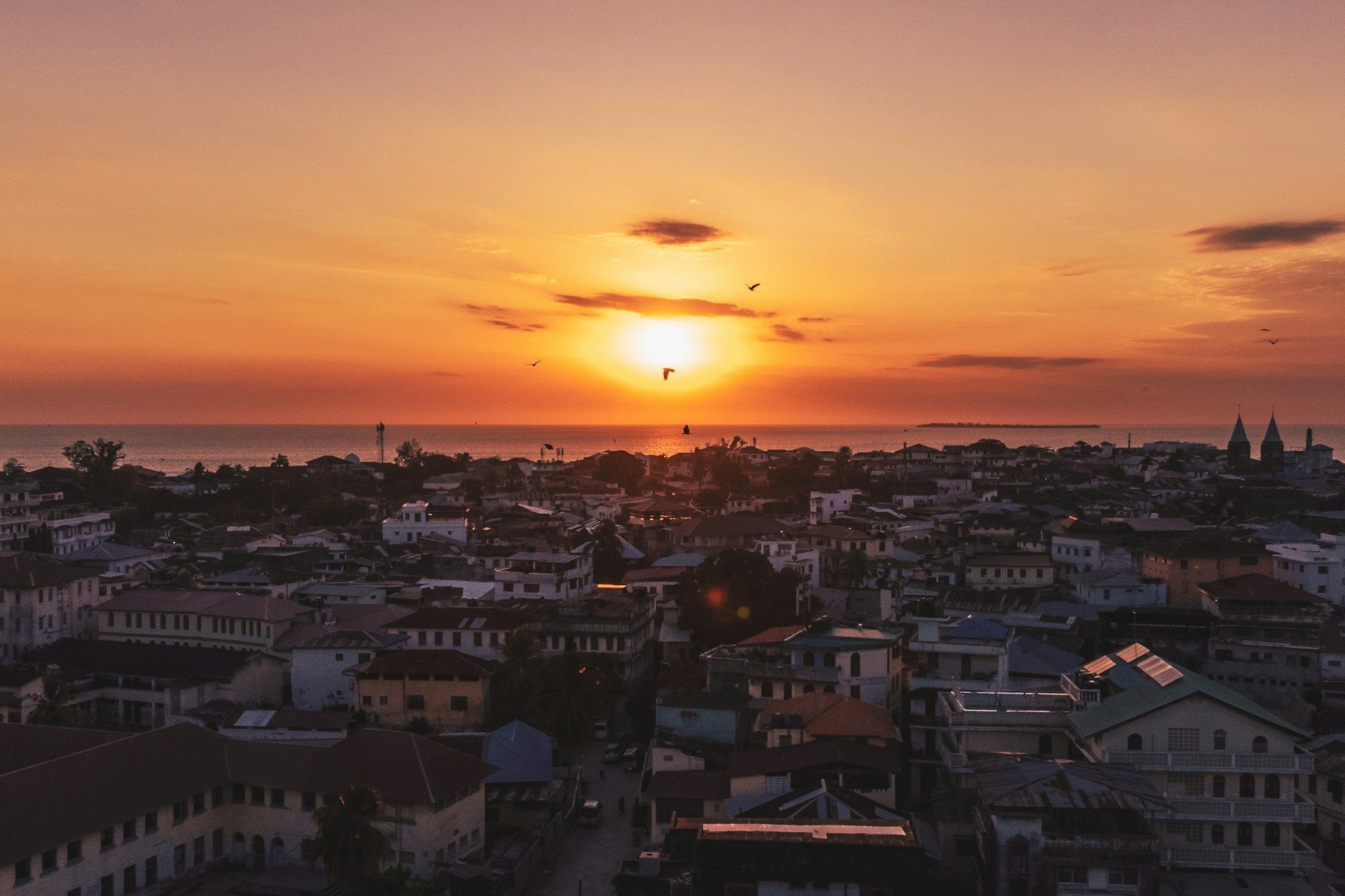 Un tramonto arancione sull'oceano illumina i tetti di una città di mare.
