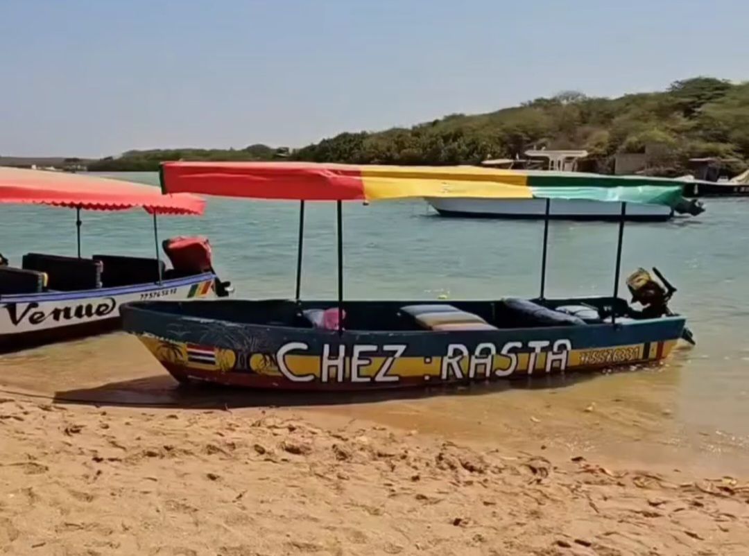 Un bote colorido con un toldo rojo, amarillo y verde está amarrado en una playa de arena junto al agua.