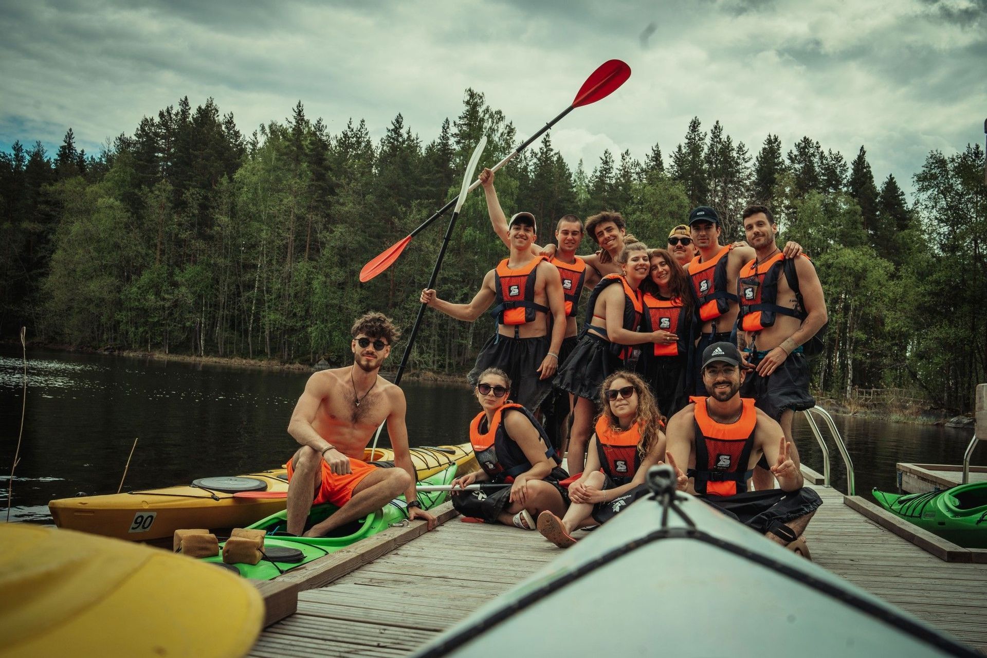 Eine WeRoad-Gruppe in orangefarbenen Schwimmwesten posiert mit ihren Kajaks für ein Foto auf einem Holzsteg.