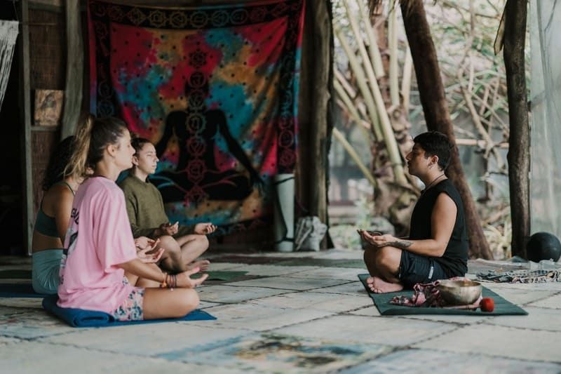 Un groupe WeRoad est assis en tailleur sur des tapis, méditant lors d'un cours de yoga dirigé par un instructeur.