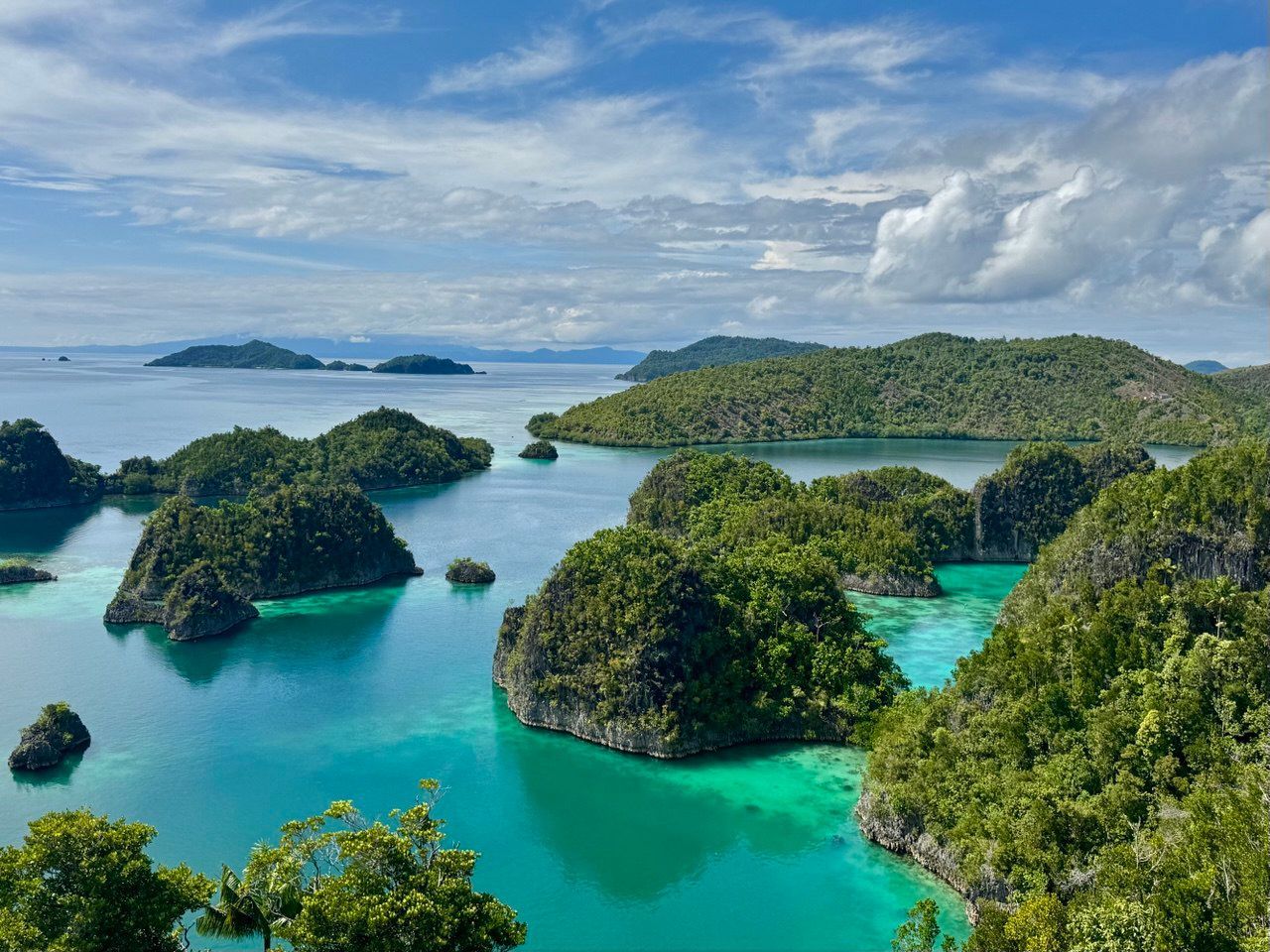 Una vista dall'alto di molte piccole isole coperte dalla giungla sparse in un oceano turchese sotto un cielo blu con nuvole bianche.