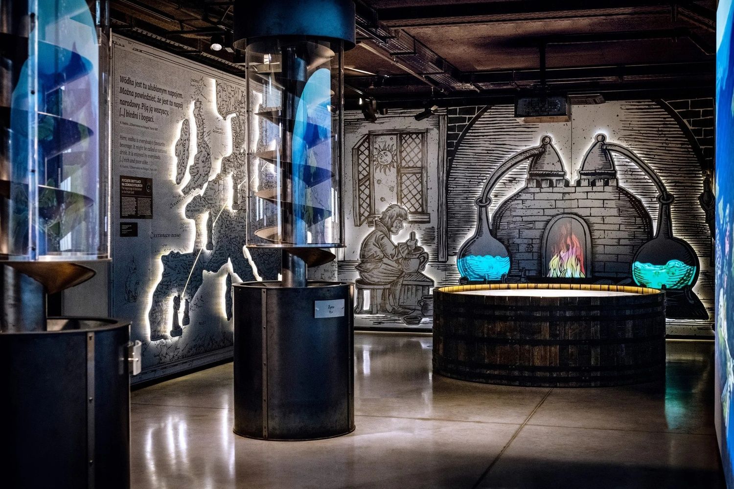 Un'esposizione in un museo della distilleria con allestimenti moderni e un murale illuminato che raffigura un antico laboratorio alchemico.