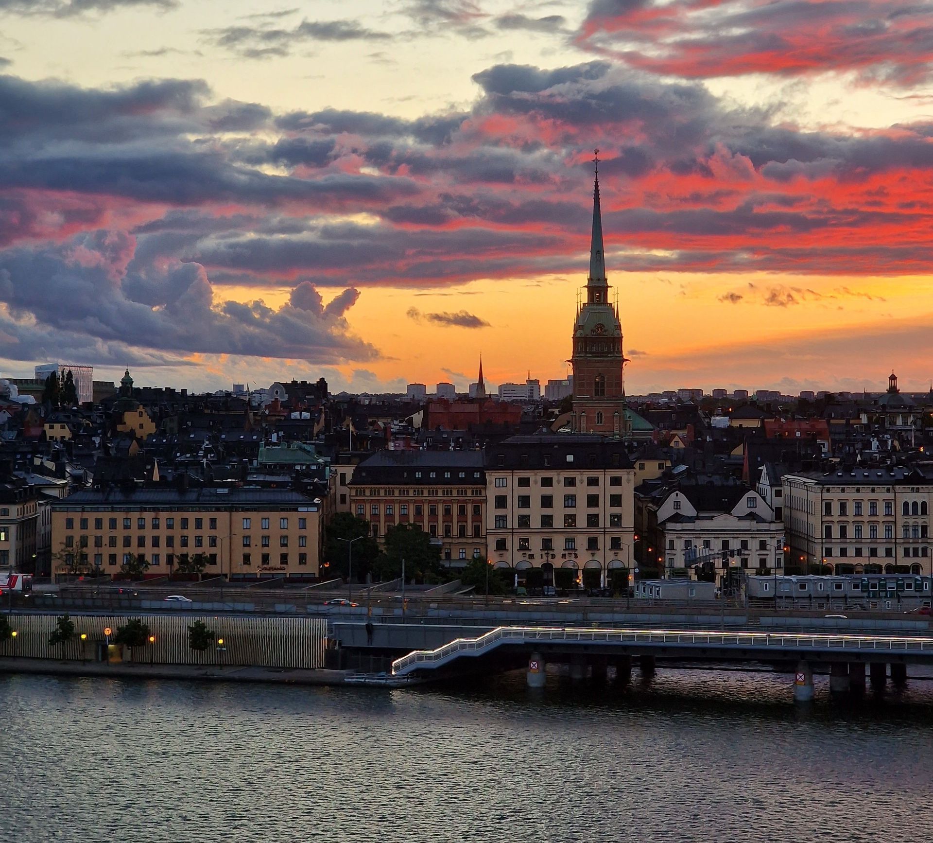 Il profilo di una città con un alto campanile di chiesa si staglia contro un tramonto colorato su uno specchio d'acqua.