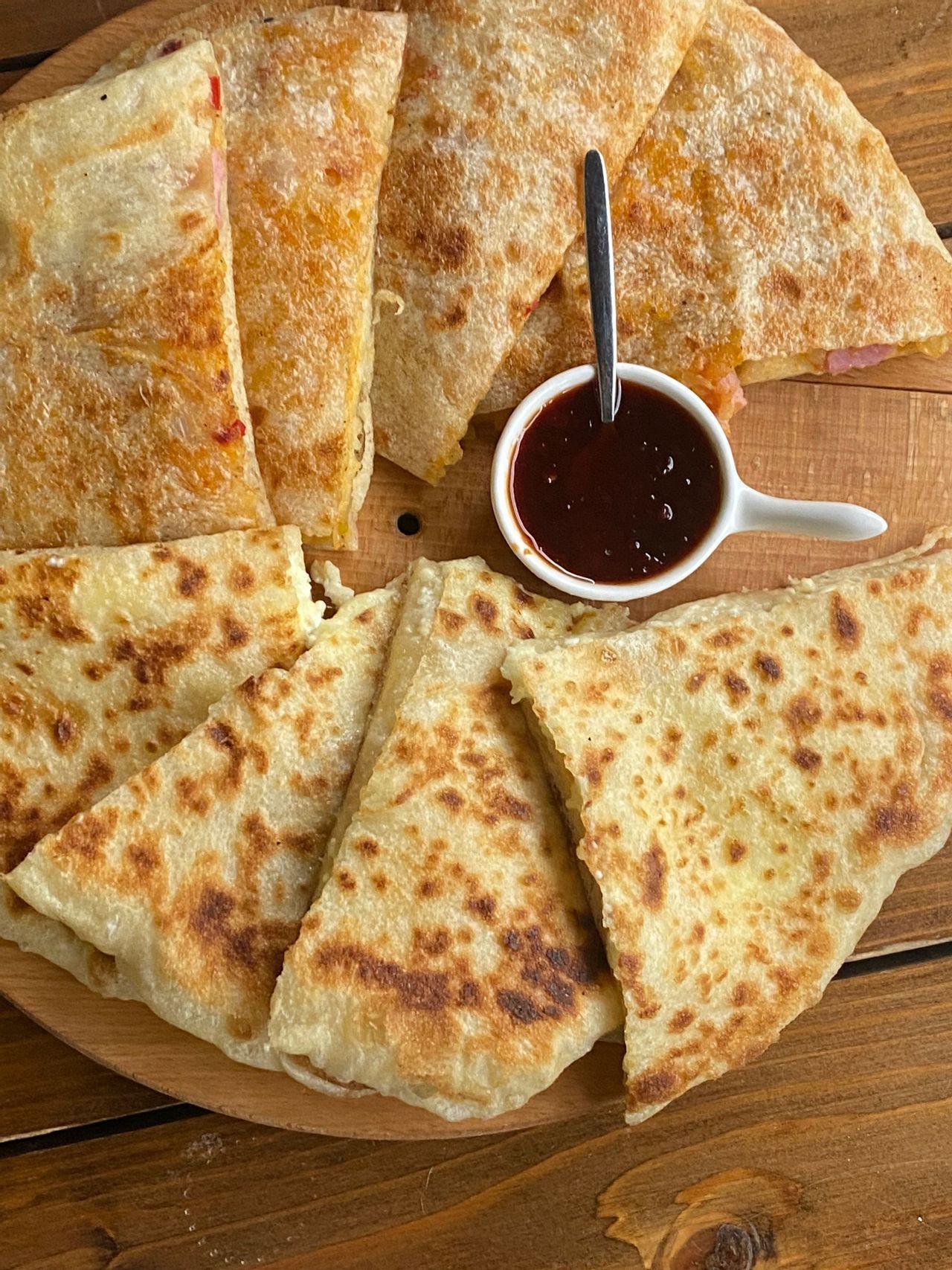 Quesadillas tostadas cortadas en triángulos y dispuestas en una tabla de madera con un pequeño tazón de salsa para mojar.
