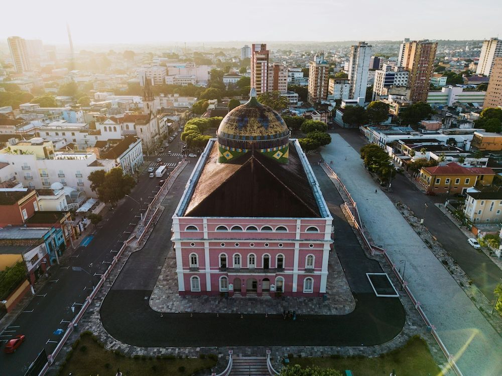 Vista aerea di un grande edificio rosa con una cupola colorata nel centro di una piazza cittadina al tramonto.