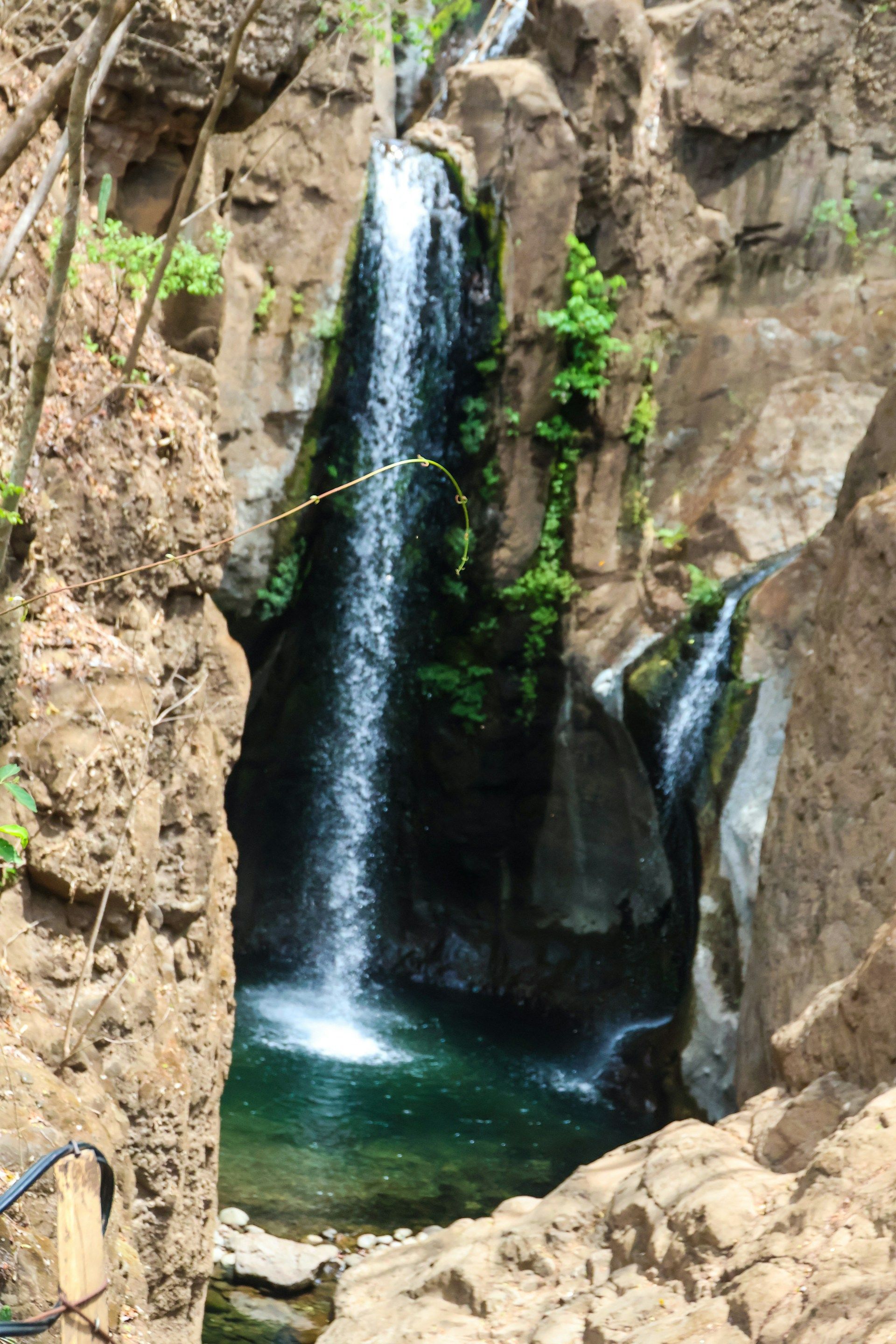 Una cascata scende da una ripida parete rocciosa, incorniciata dalle pareti del canyon, in una piccola pozza d'acqua turchese.