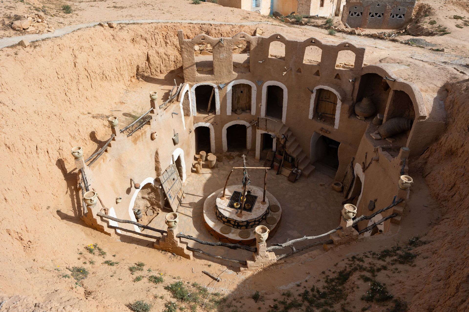 Una vista dall'alto di un'abitazione sotterranea circolare in terra, con cortile centrale, un pozzo e ingressi ad arco.