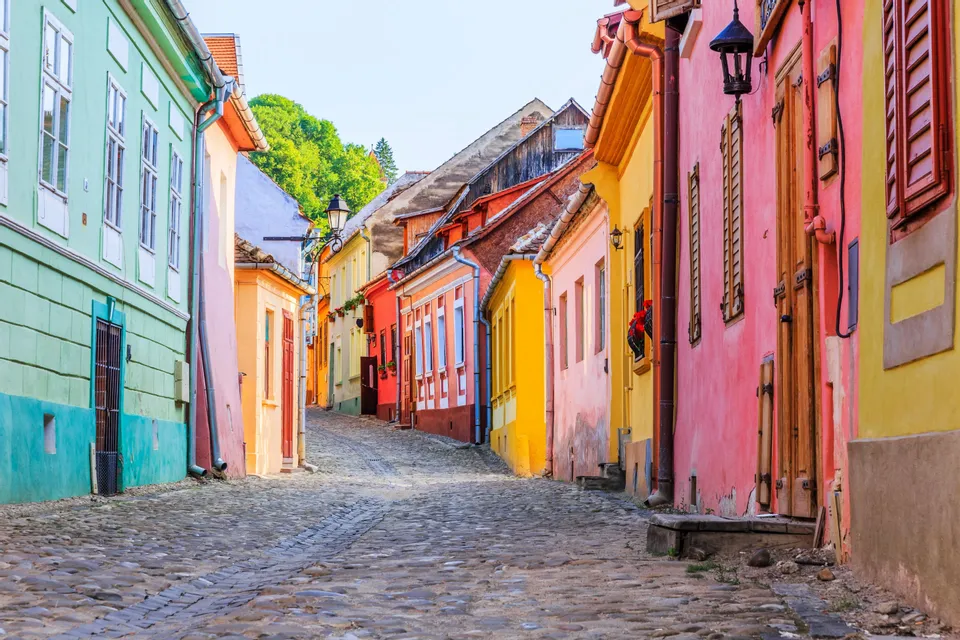 Una estrecha calle empedrada y vacía serpentea cuesta arriba, flanqueada por edificios históricos de colores vivos bajo un cielo despejado.