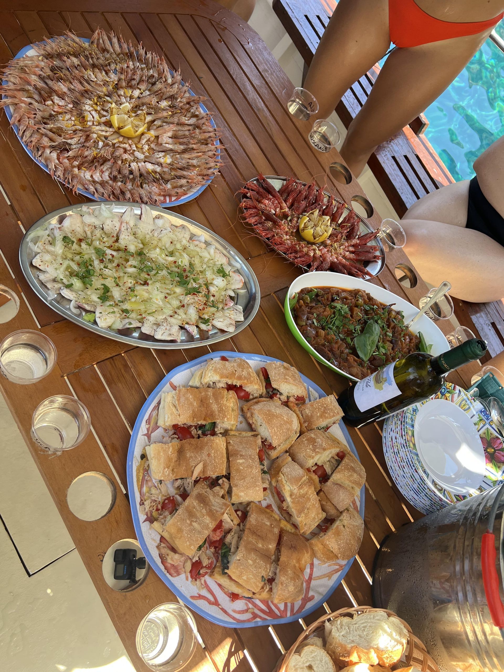 Un gruppo WeRoad in viaggio cena in barca, con una tavola imbandita di frutti di mare freschi, panini e vino bianco.