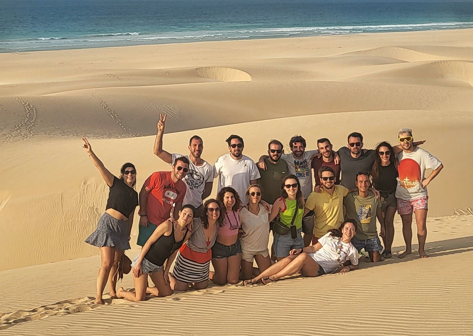 Un viaje en grupo de WeRoad posando juntos para una foto en dunas de arena, con el océano visible al fondo.