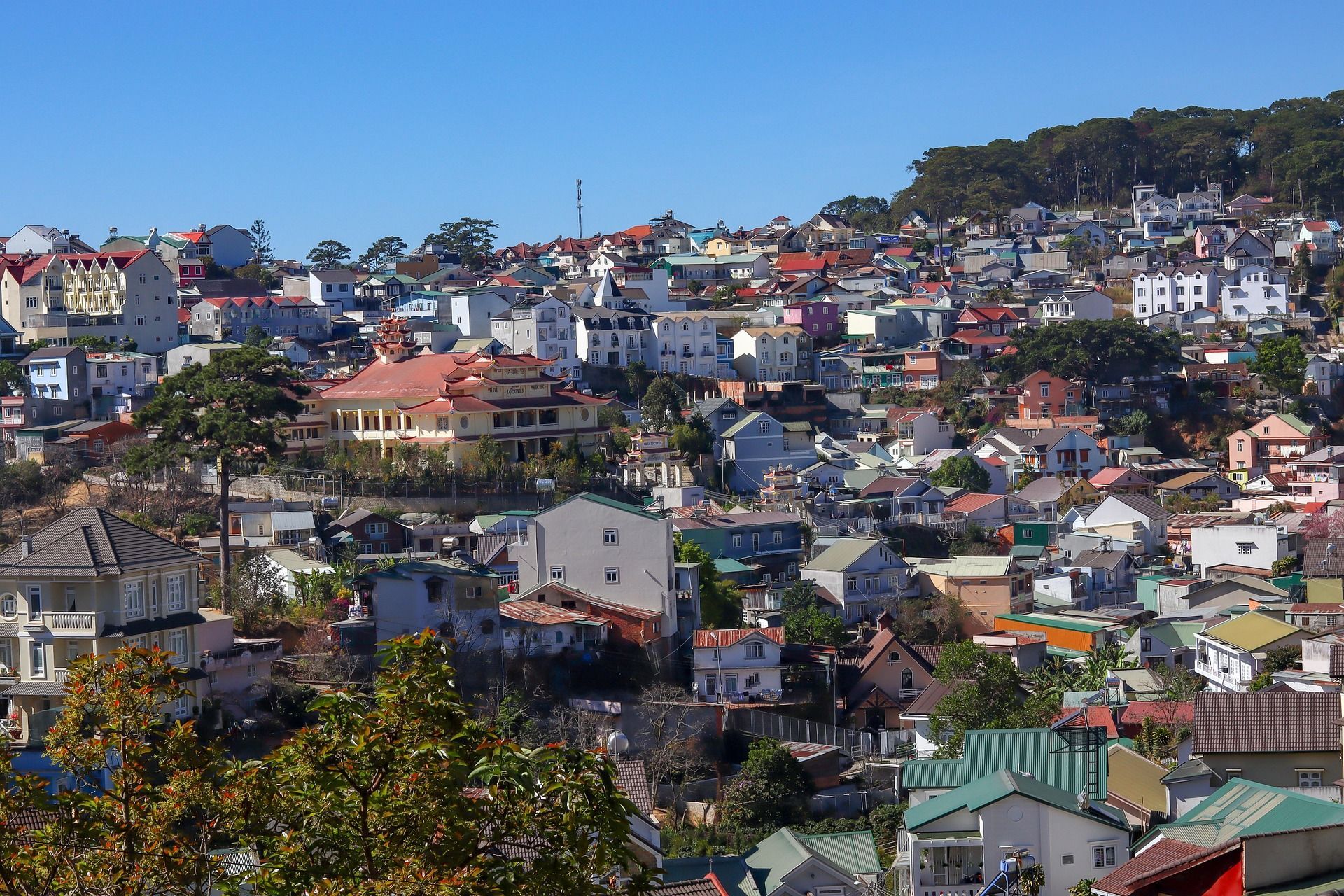 Un'ampia veduta di un borgo collinare fittamente costruito, con case e palazzi colorati sotto un cielo azzurro e limpido.