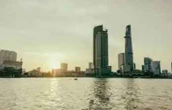 Il sole tramonta dietro un moderno skyline di grattacieli, visto da uno specchio d'acqua.