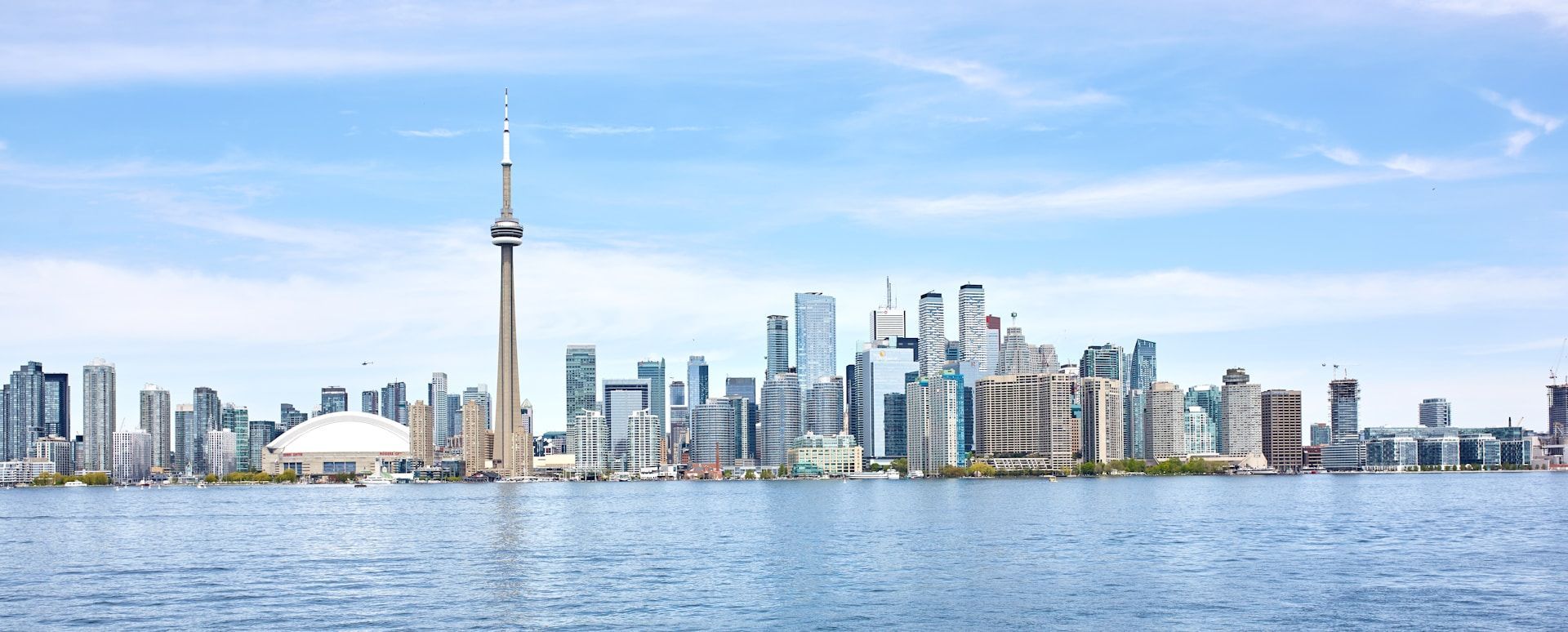 Uno skyline moderno con un'alta torre di osservazione e grattacieli, visibile dall'acqua sotto un cielo azzurro e limpido.