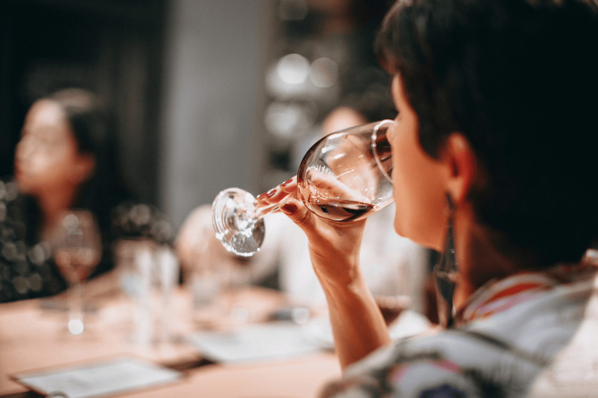 Una persona con capelli corti e scuri beve vino rosso da un bicchiere mentre è seduta a un tavolo durante un viaggio di gruppo WeRoad.