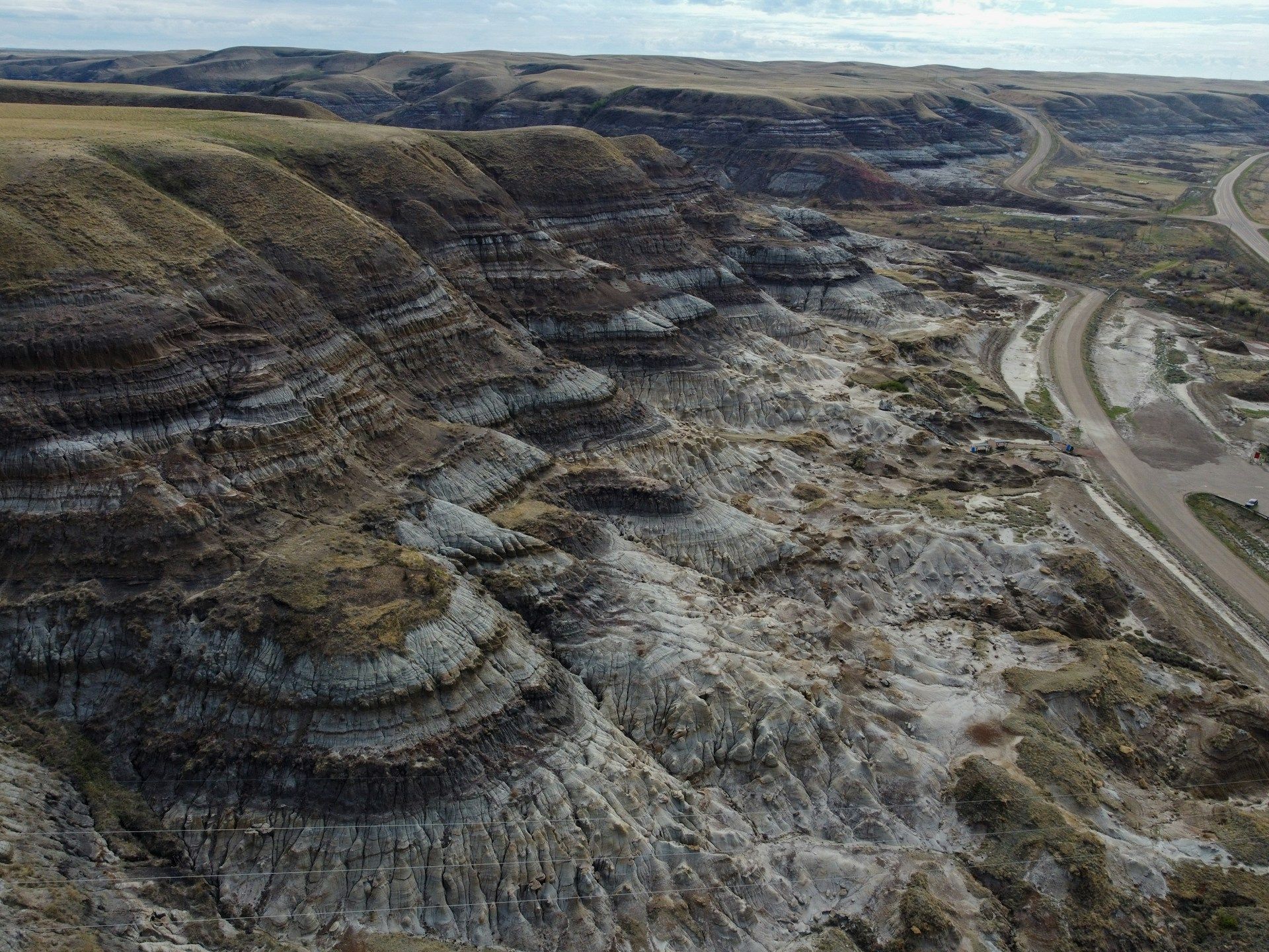 Una veduta aerea di un vasto paesaggio di calanchi, con colline erose che mostrano strati sedimentari visibili e una strada tortuosa.