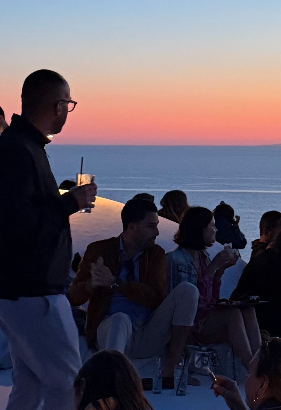 Un viaggio di gruppo WeRoad con persone che socializzano su una terrazza ammirando il tramonto sul mare.