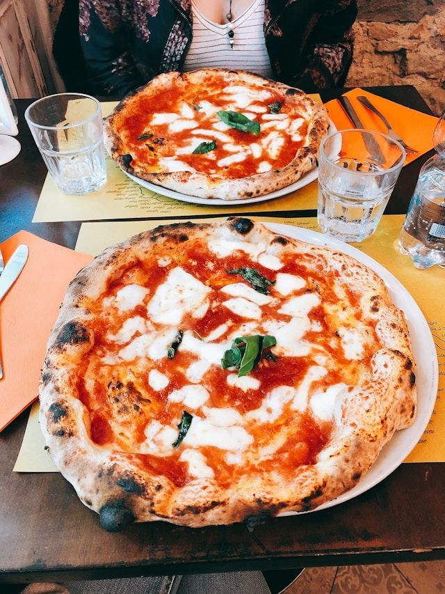 Deux pizzas napolitaines garnies de mozzarella fraîche et de basilic posées sur une table de restaurant avec des verres d'eau.