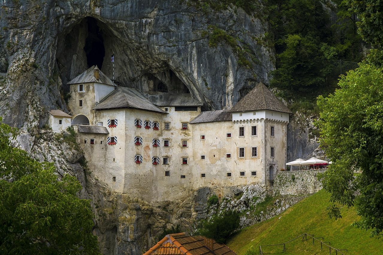Un grande castello bianco, incastonato direttamente all'imbocco di una grotta buia su una parete rocciosa a picco, circondato da una lussureggiante vegetazione verde.
