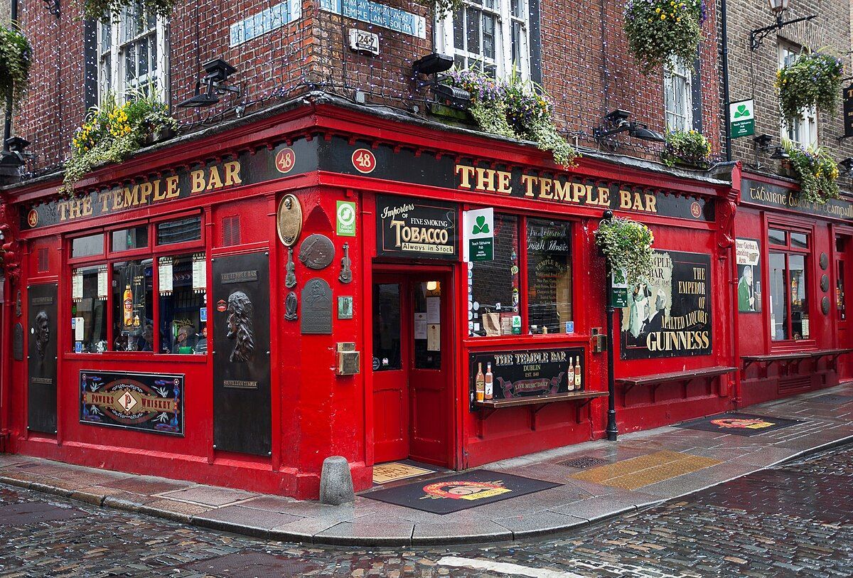 La facciata ad angolo rosso acceso del pub The Temple Bar su una strada di ciottoli bagnata.