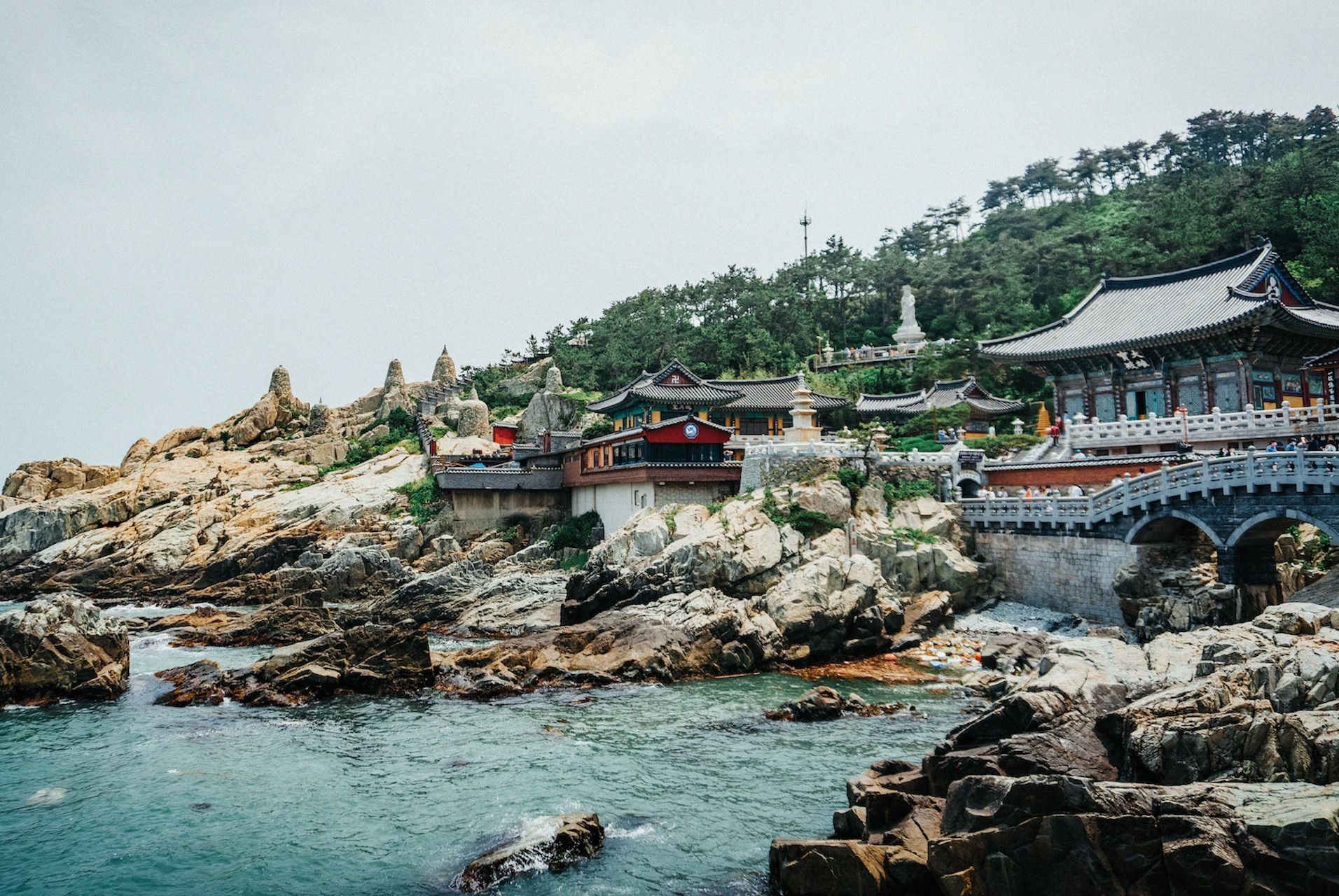 Un complesso di templi asiatici tradizionali con un ponte di pietra, costruito su una scogliera rocciosa a picco sul mare.