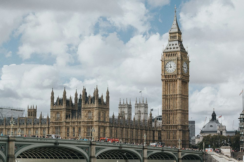 La torre dell'orologio del Big Ben e le Houses of Parliament si ergono dietro un ponte trafficato sotto un cielo nuvoloso.