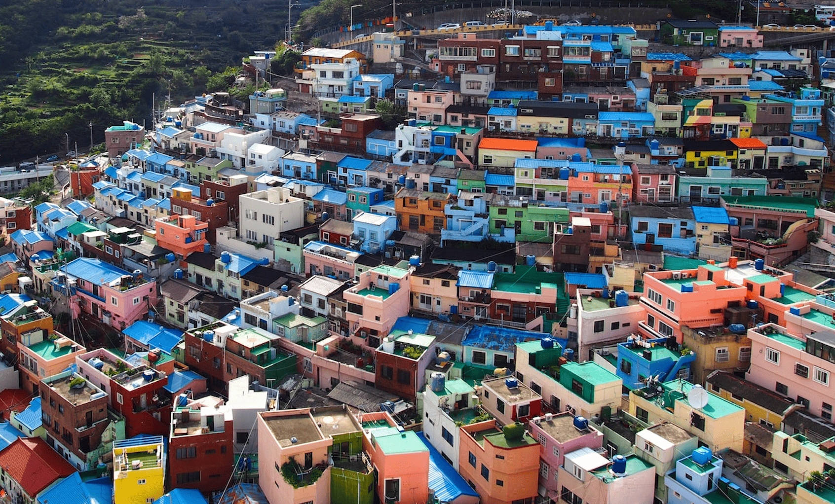 Un fitto raggruppamento di case colorate con tetti blu brillanti, edificate su un ripido versante verde, di giorno.