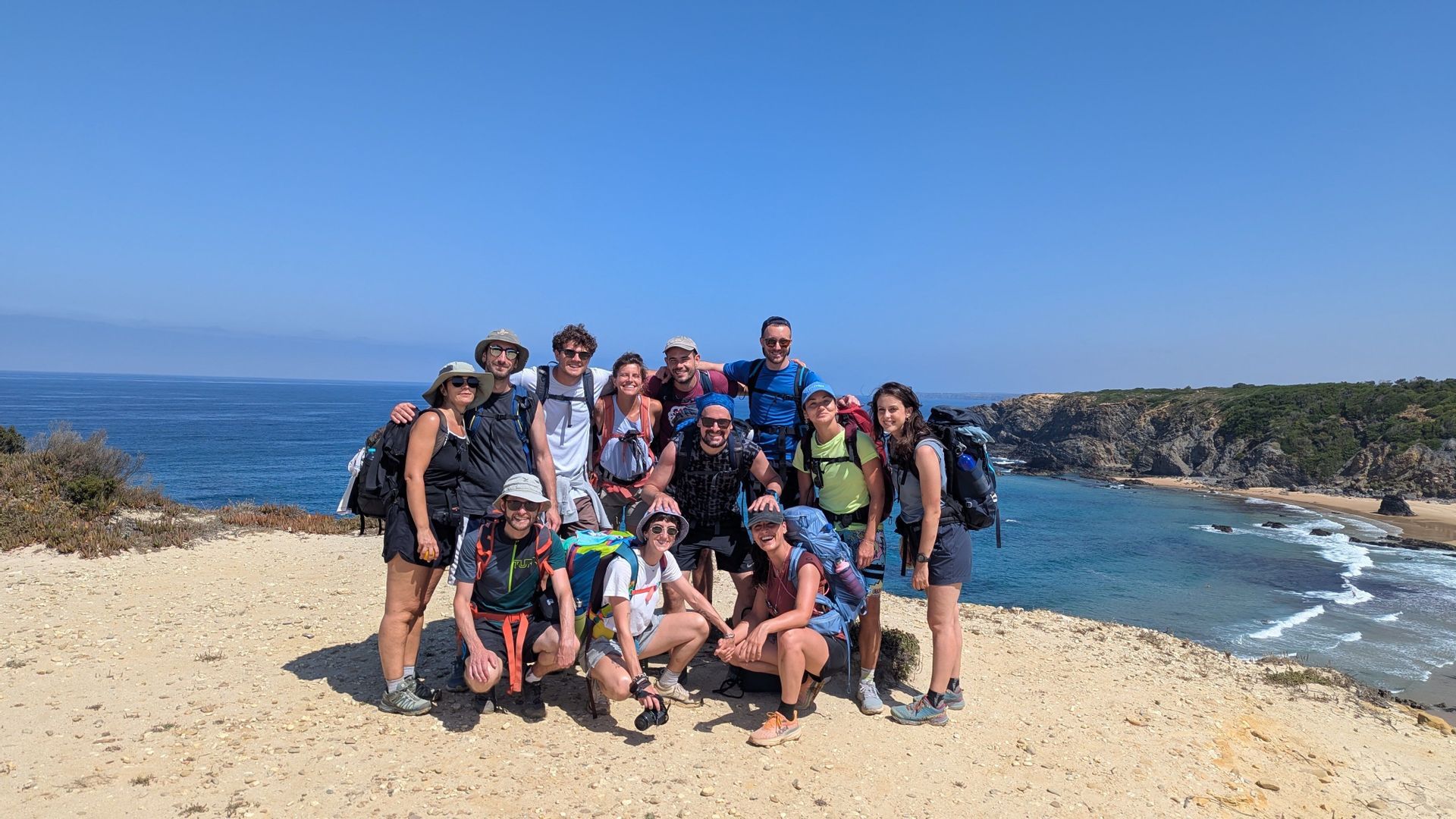 Un viaggio di gruppo WeRoad con zaini da trekking posa per una foto su una scogliera soleggiata a picco sull'oceano.