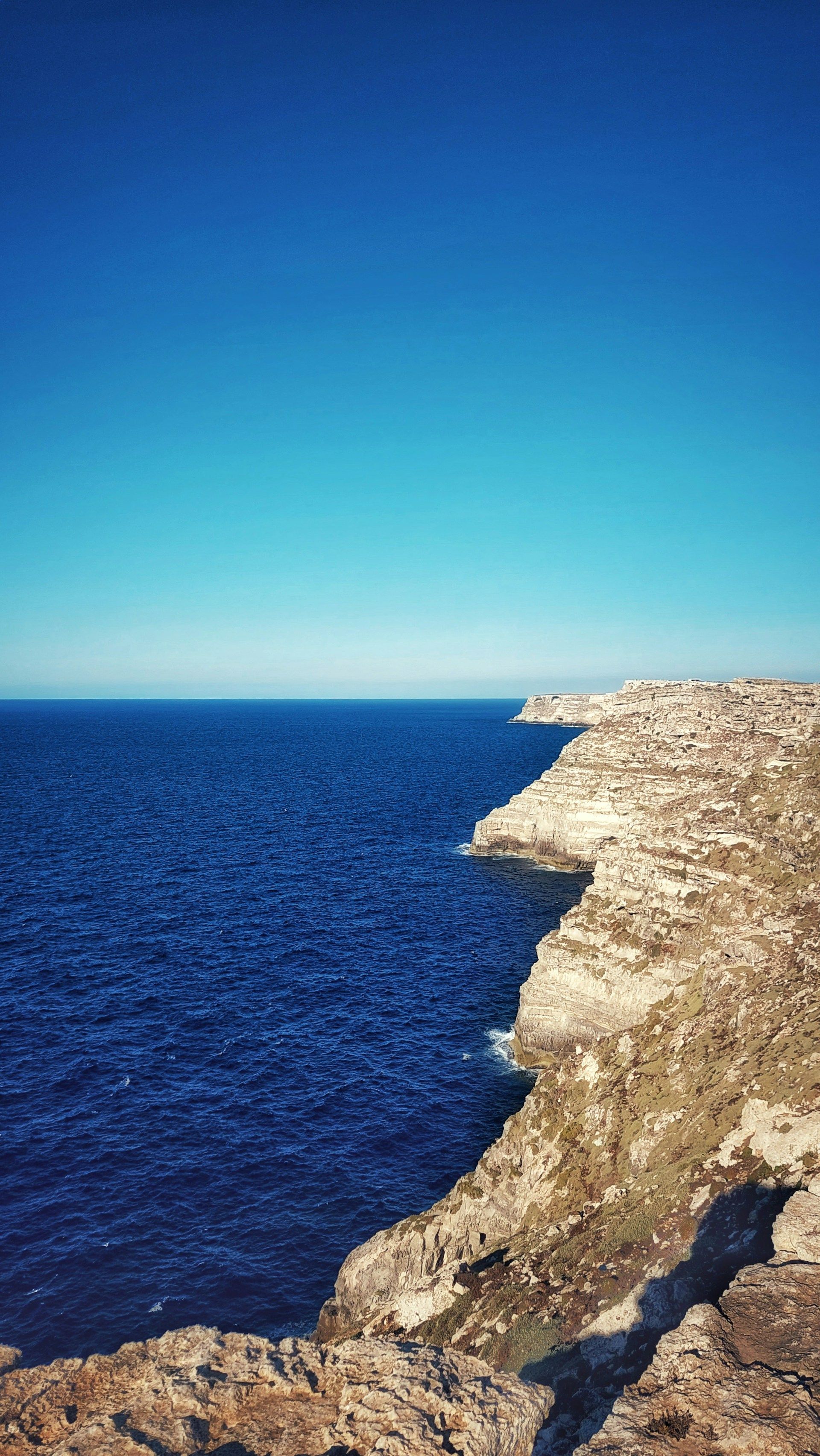 Una veduta dall'alto di aspre scogliere chiare che si affacciano su un mare blu profondo sotto un cielo azzurro limpido.