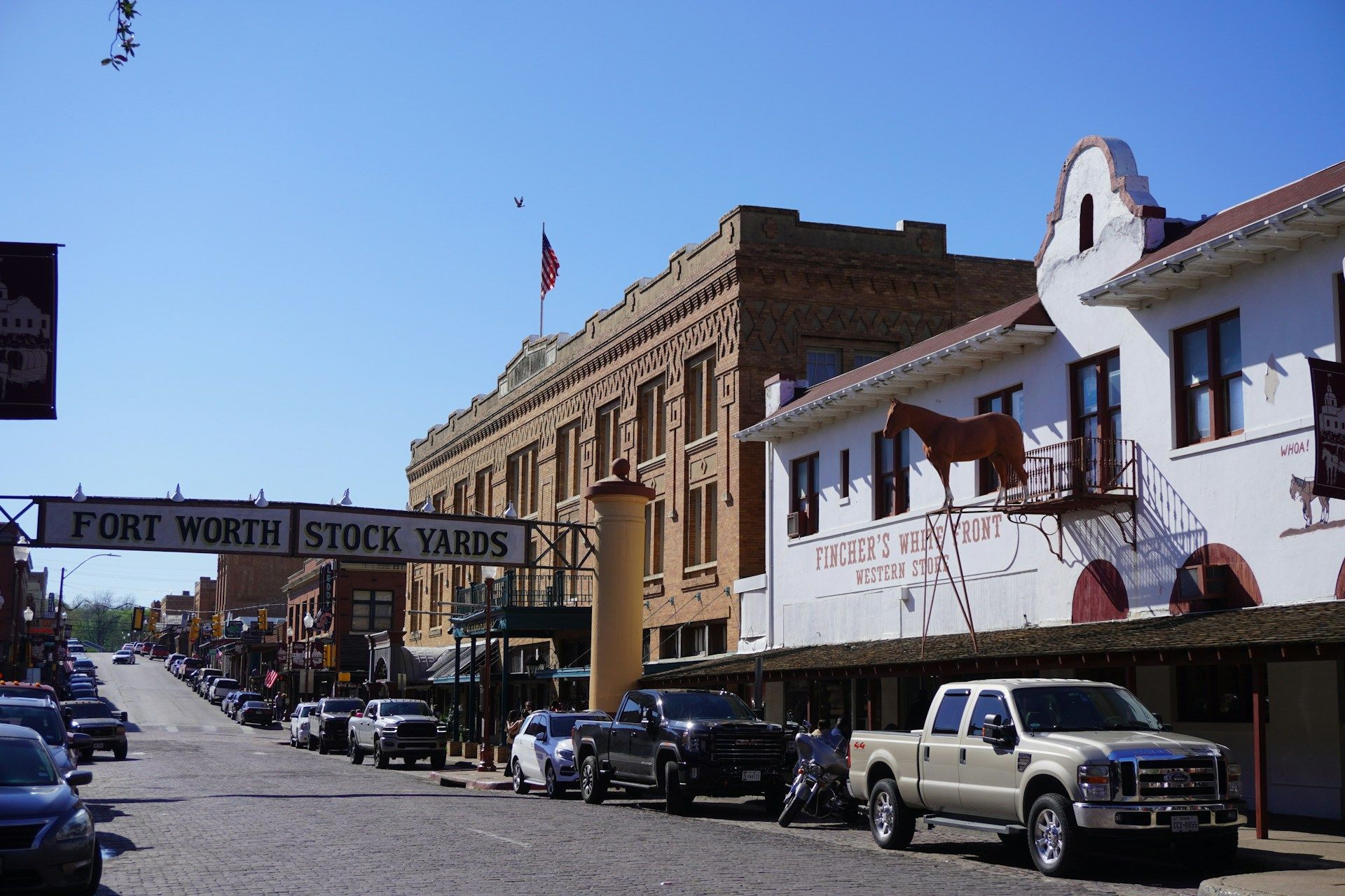 Il cartello d'ingresso dei Fort Worth Stock Yards si inarca su una strada di ciottoli fiancheggiata da auto ed edifici in stile western.