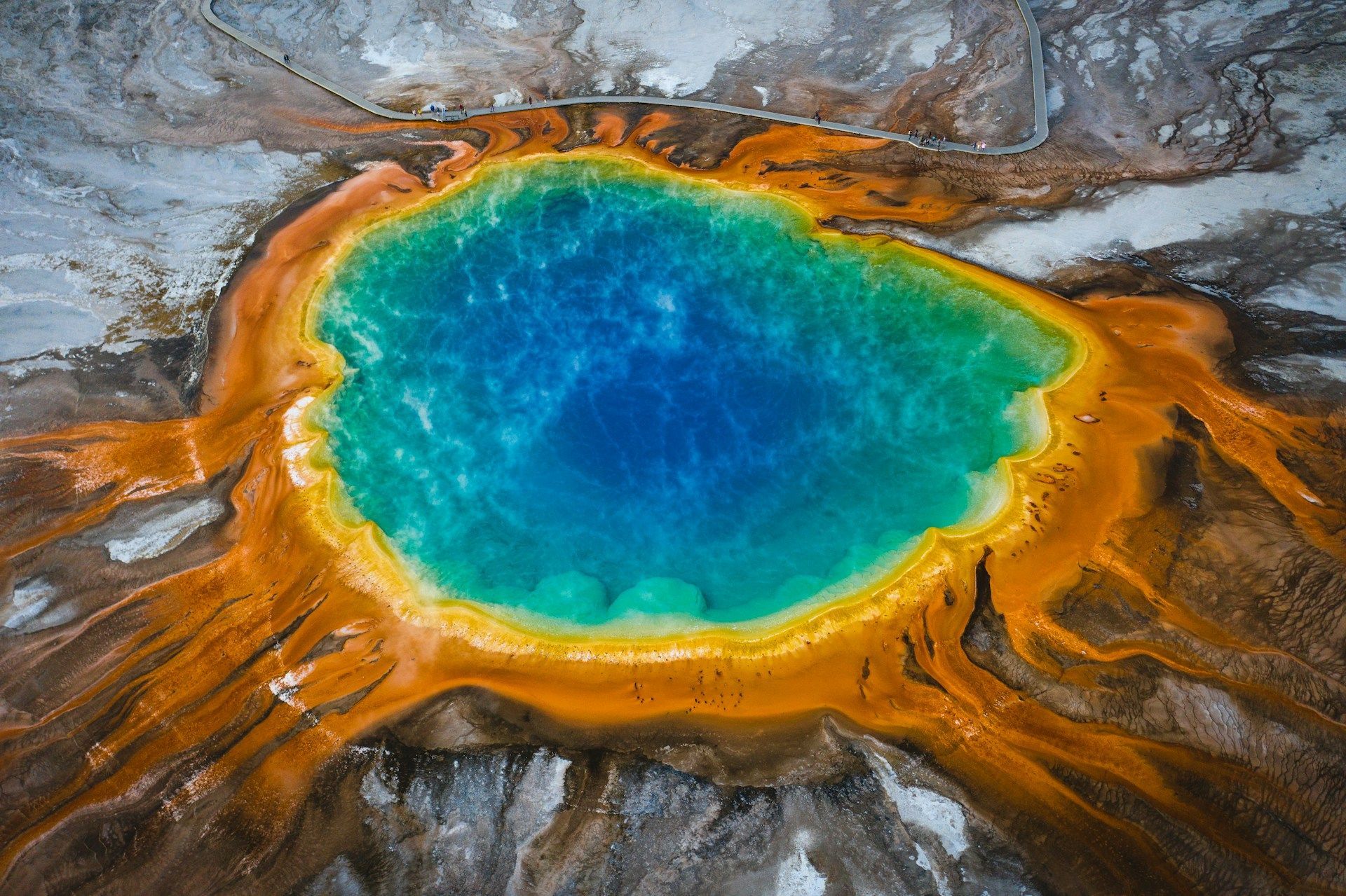 Una veduta aerea dall'alto di una sorgente geotermica con acqua blu vivace, circondata da anelli minerali arancioni e gialli brillanti.