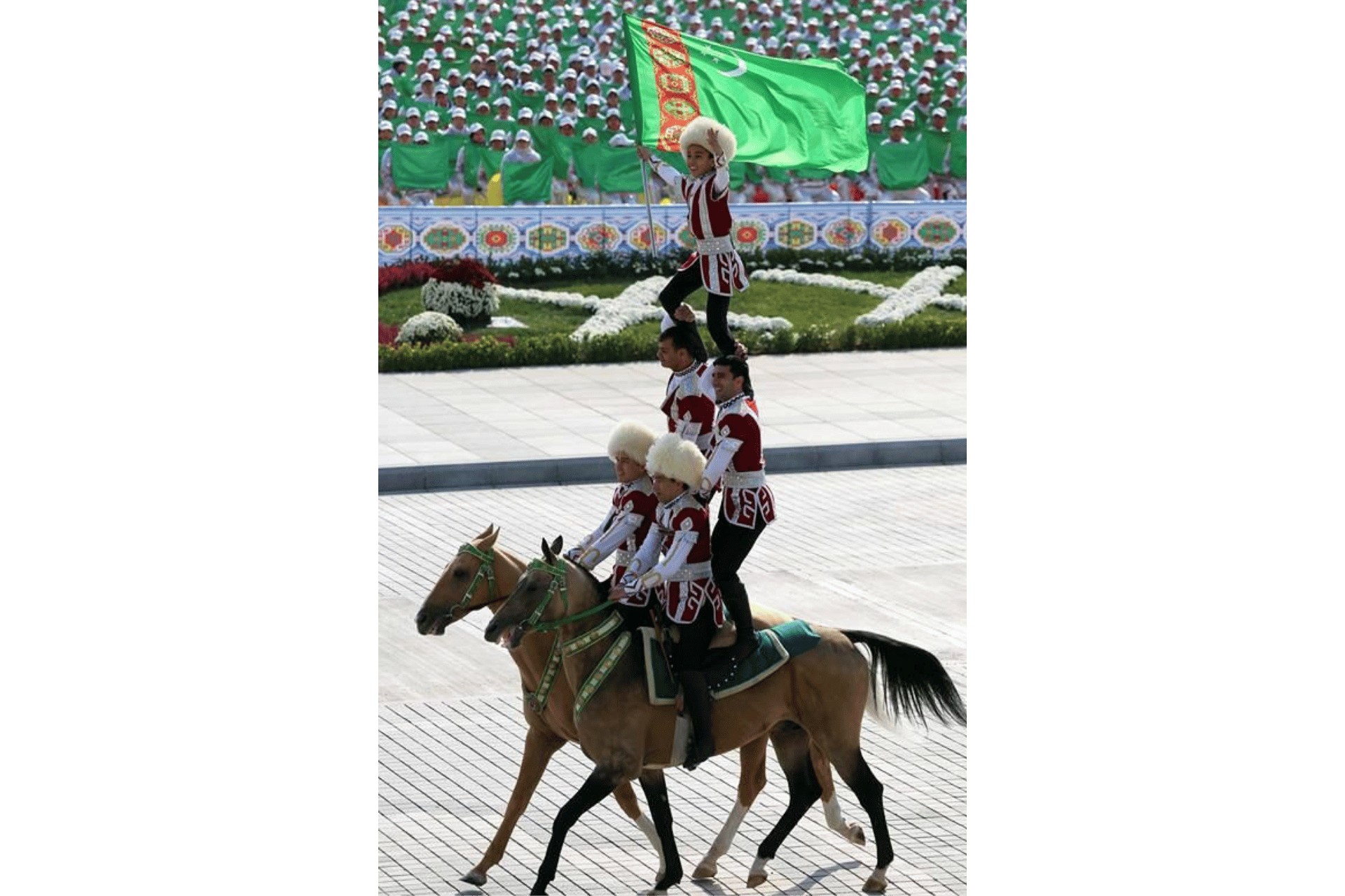 Un bambino sventola la bandiera del Turkmenistan dalla cima di una piramide umana formata da artisti equestri in abiti tradizionali.