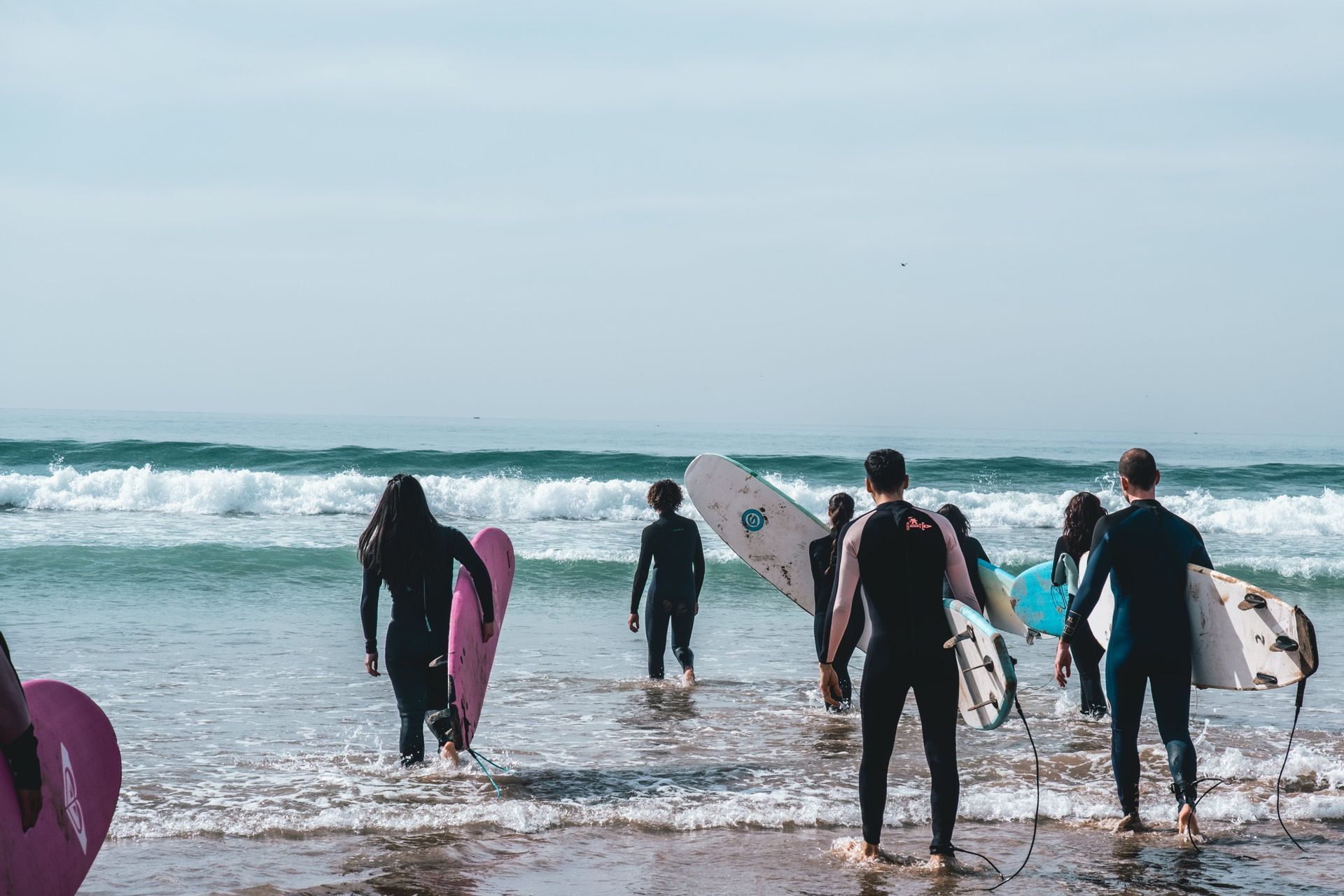 Un viaggio di gruppo WeRoad di surfisti in muta che trasportano le loro tavole e camminano tra le onde dell'oceano.