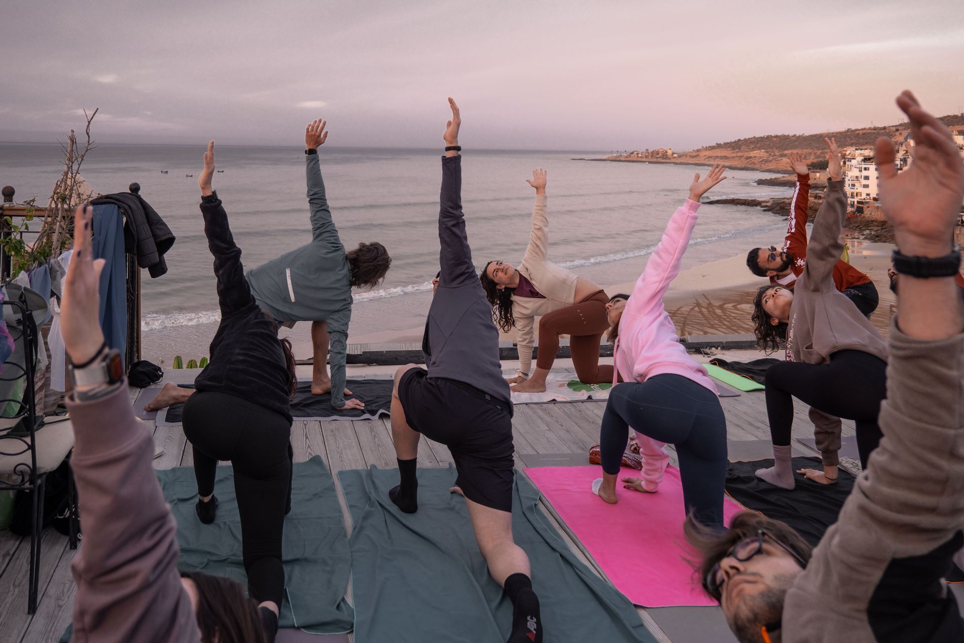 Un gruppo WeRoad pratica yoga su un pontile di legno con vista su spiaggia e oceano all'alba.
