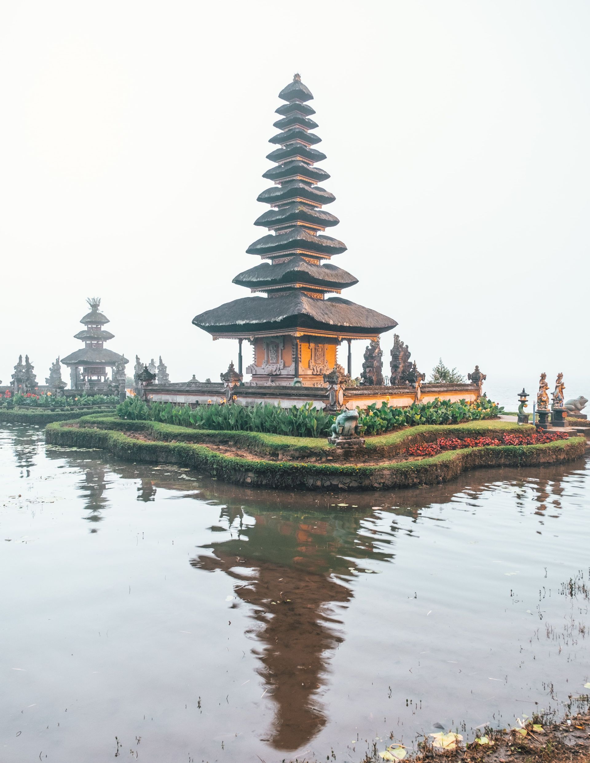 Un tempio asiatico a più livelli su una piccola isola circondata da acque calme, con il suo riflesso visibile in una giornata nebbiosa.
