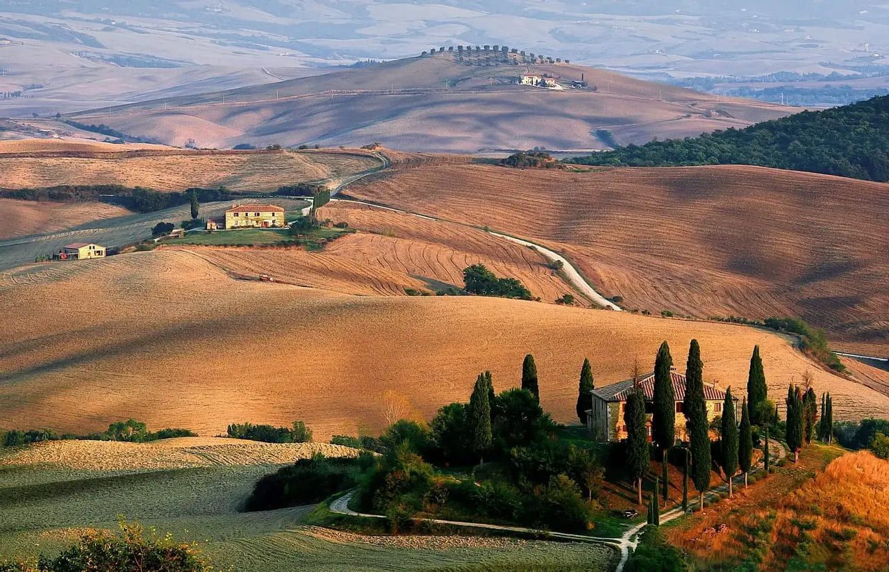 Una vista suggestiva di ville e cipressi sparsi su dolci colline dorate sotto un cielo velato.