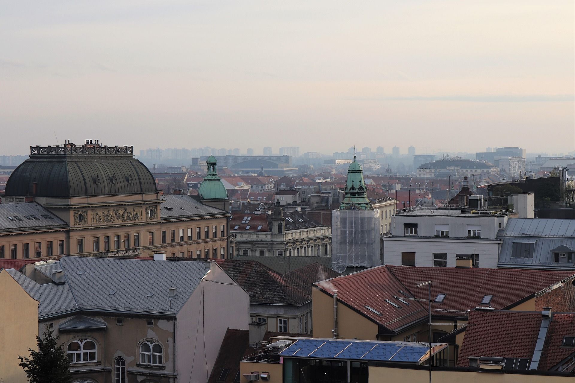 Vista sopraelevata sui tetti di una città, con cupole e guglie in evidenza sotto un cielo velato.