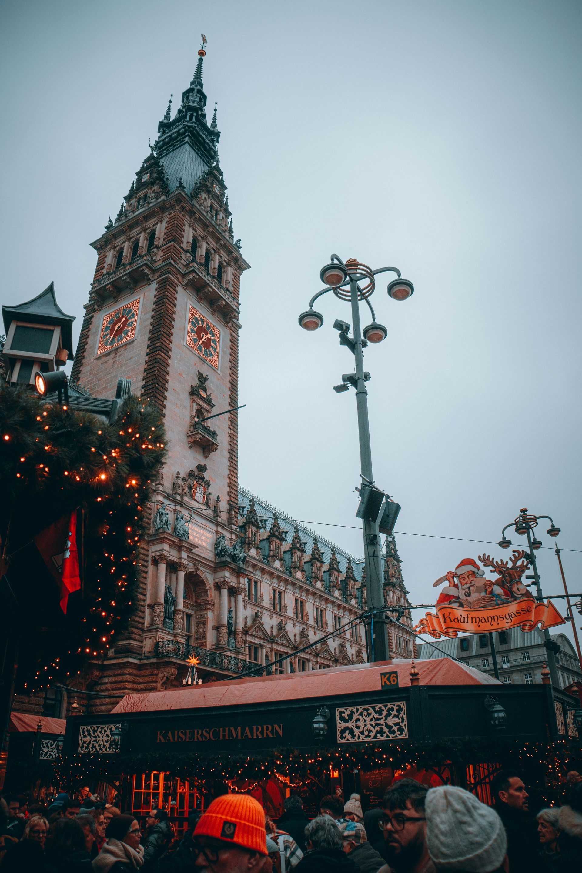 La folla si riunisce in un mercatino di Natale all'aperto con bancarelle di cibo decorate di fronte a una storica torre dell'orologio.